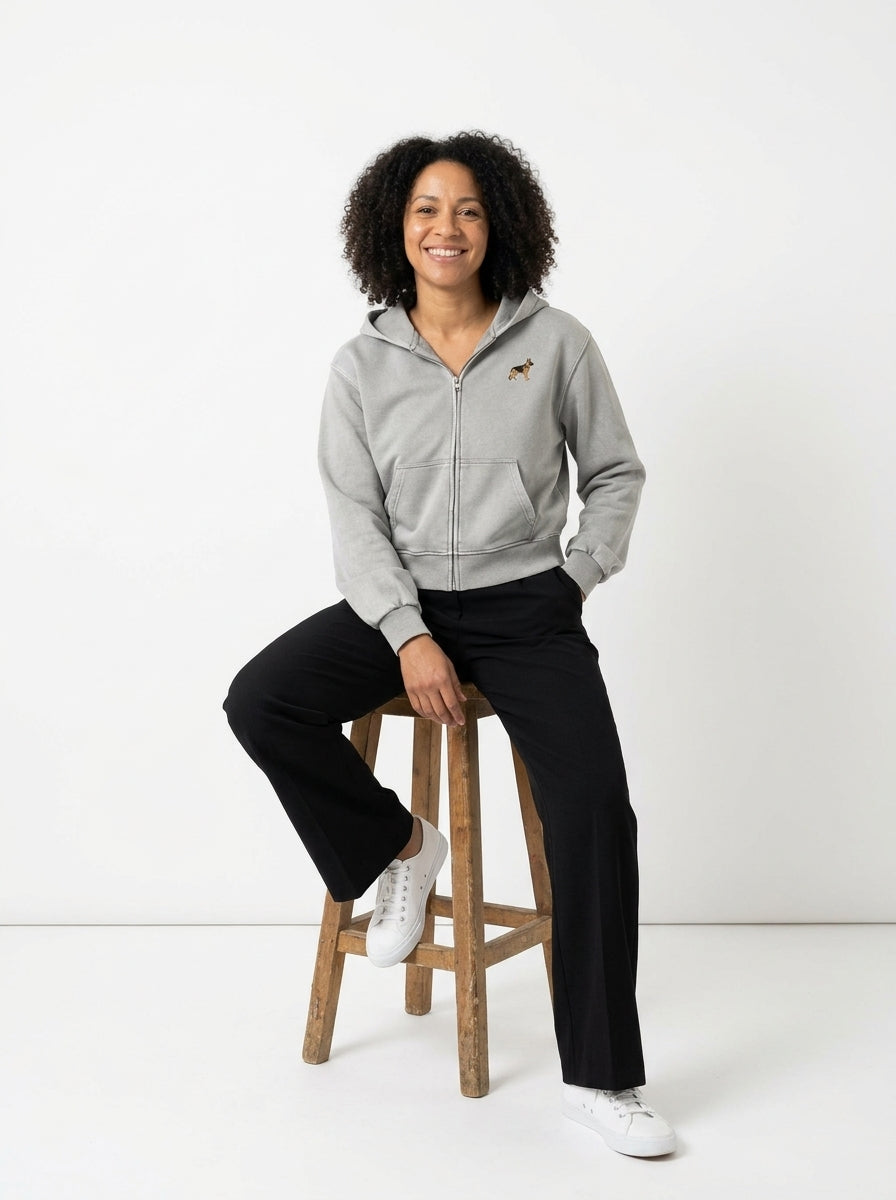Woman sitting on a stool in the Light Grey mineral wash zip hoodie with a small embroidered-look German Shepherd on the chest
