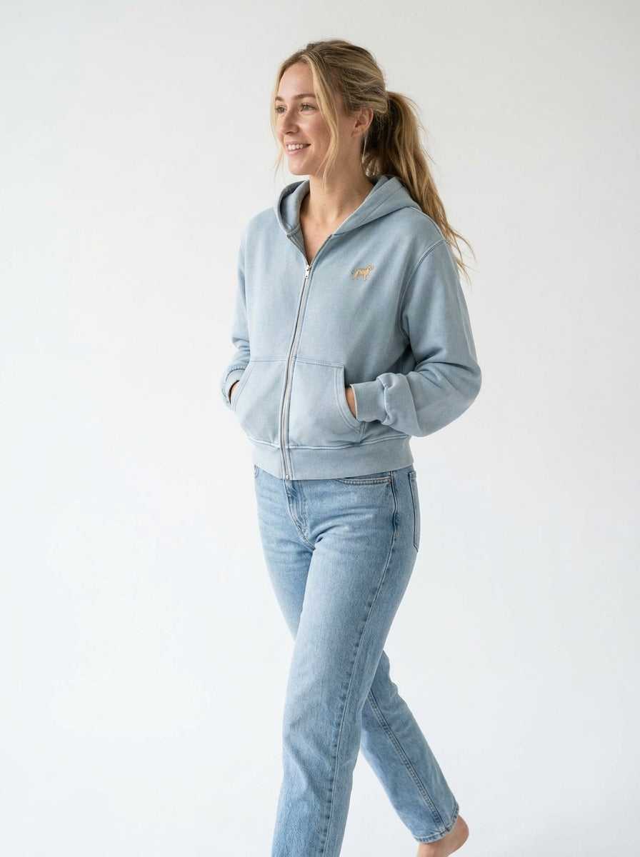 Woman walking in the Haze Blue mineral wash zip hoodie with a small embroidered-look Labrador on the chest